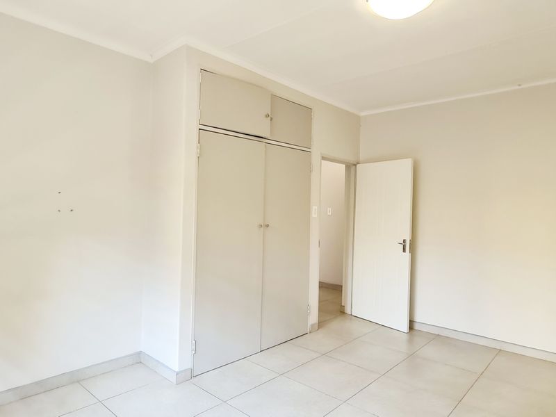An empty bedroom featuring neutral tiled flooring, built-in cupboards with overhead storage, and clean white walls ready for personalization.
