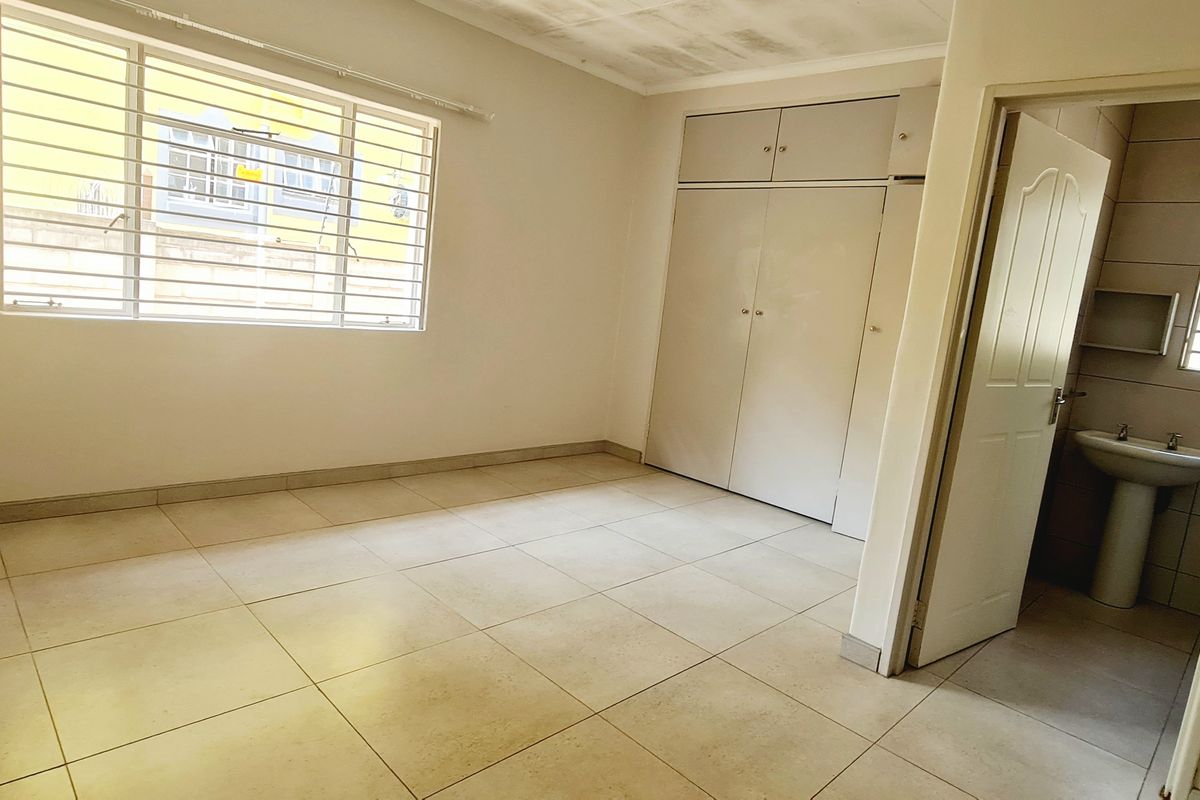 An empty bedroom featuring tiled flooring, built-in cupboards, and an adjoining en-suite bathroom with a pedestal basin.