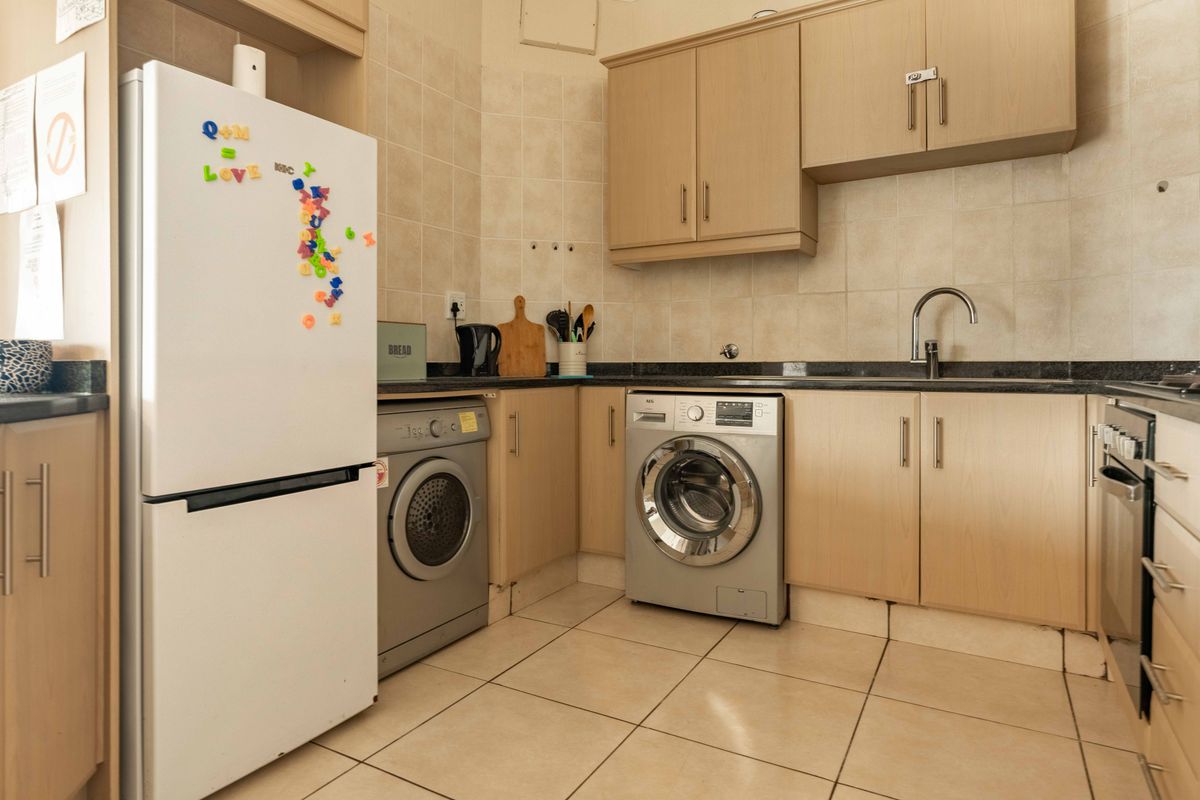 Functional kitchen featuring light wood-finish cabinetry, tiled backsplash, granite-look countertops, and integrated laundry appliance connections.