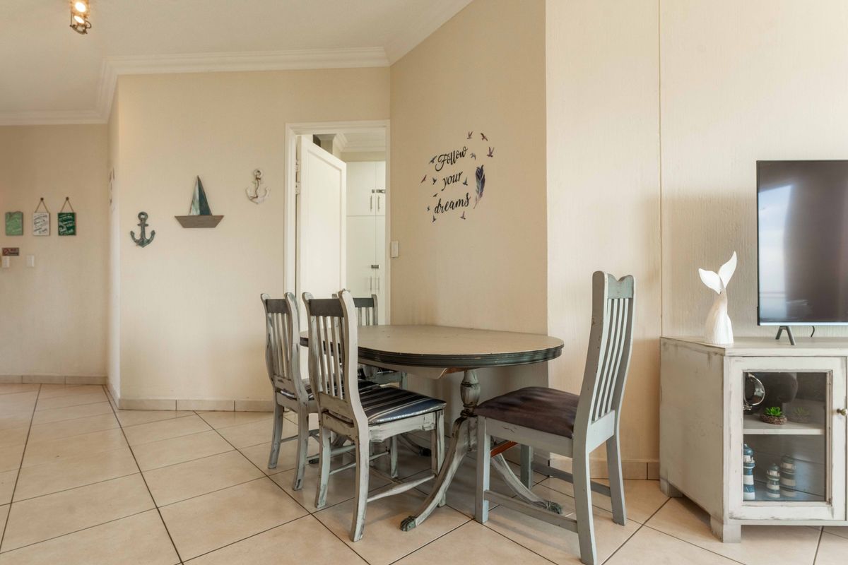 A living area featuring neutral tiled flooring and coved cornicing, providing a functional space with access to an adjacent room.