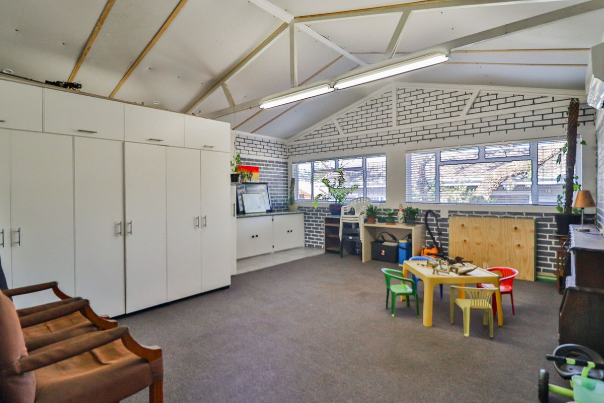 Spacious living area featuring exposed roof trusses, painted brick walls, built-in storage cabinetry, and large aluminium windows providing ample natural light.