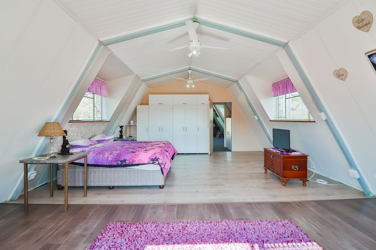 Spacious attic-style bedroom featuring a vaulted ceiling, built-in storage cupboards, dual ceiling fans, and light-toned laminate flooring.