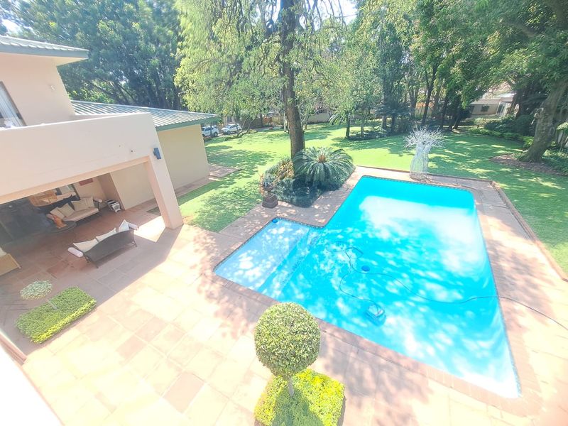 Elevated view of a swimming pool, paved patio area, and expansive landscaped garden with mature trees.