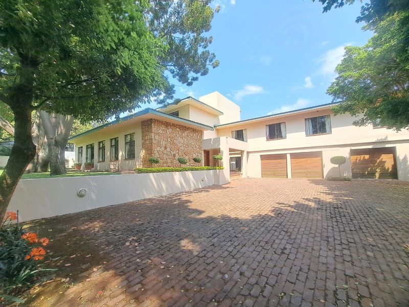 Spacious front exterior view featuring a large brick-paved driveway, stone-clad facade, and a triple garage, set within a mature, well-maintained garden.