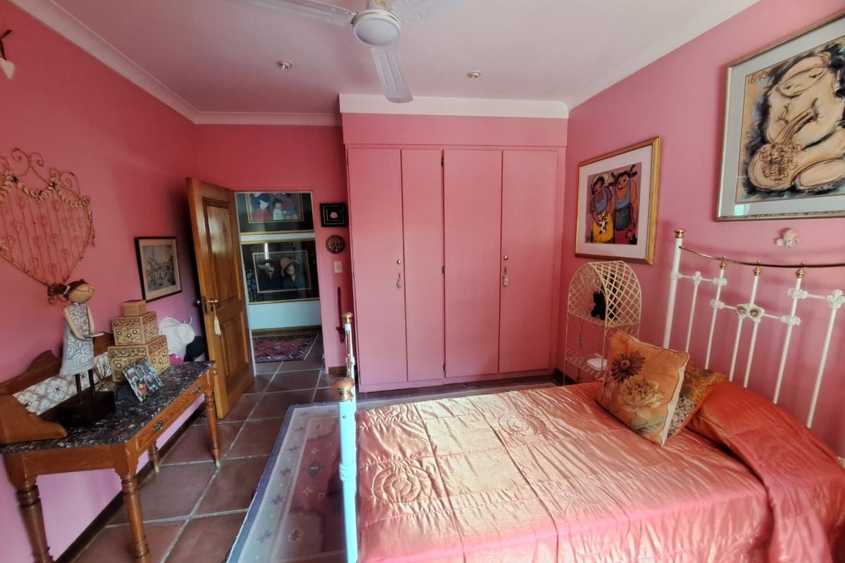 A bedroom featuring built-in wardrobes, tiled flooring, and a ceiling fan, currently finished with vibrant pink wall paint.