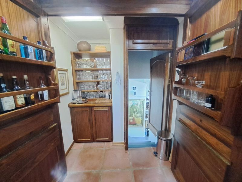 A dedicated bar area featuring extensive built-in wooden cabinetry, custom shelving, and terracotta floor tiles, leading to an adjacent room.