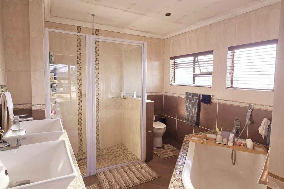 Spacious bathroom featuring a double vanity, glass-enclosed shower, and a freestanding bathtub with neutral tiled finishes throughout.