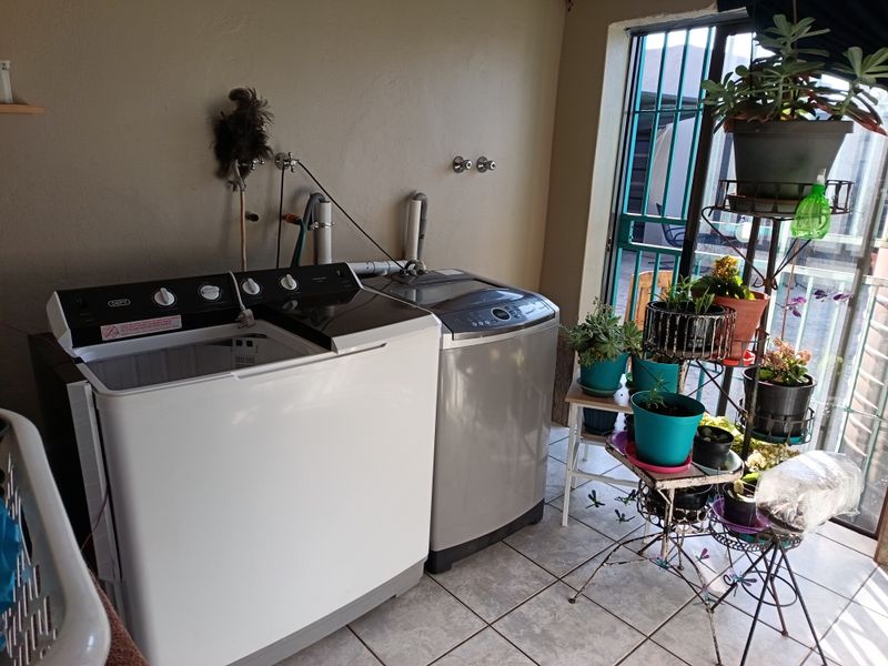 A functional laundry area featuring tiled flooring and dedicated plumbing connections for washing machines, with direct access to an outdoor area via a security gate.