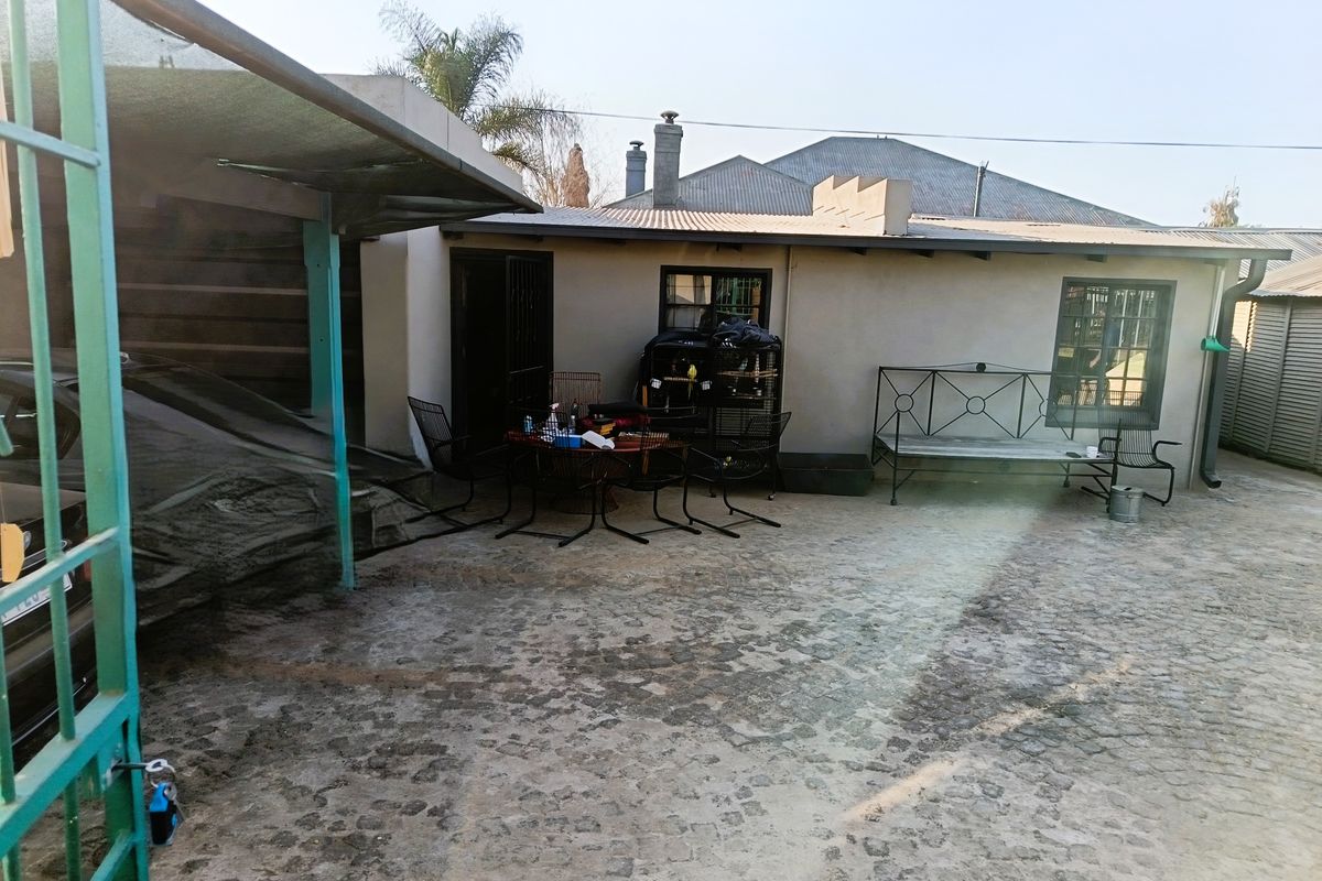 Rear exterior area featuring cobblestone paving, a covered carport, and direct access to the main dwelling structure.