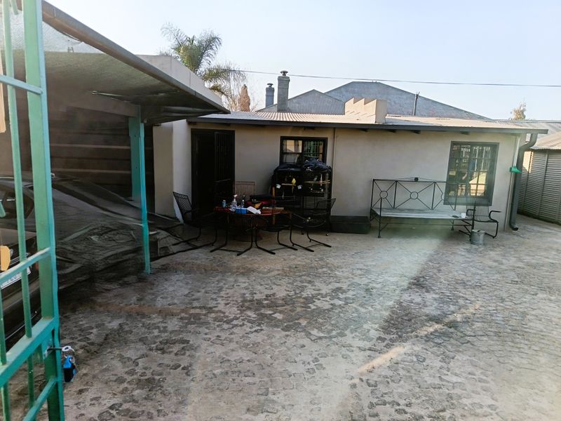 Rear exterior area featuring cobblestone paving, a covered carport, and direct access to the main dwelling structure.