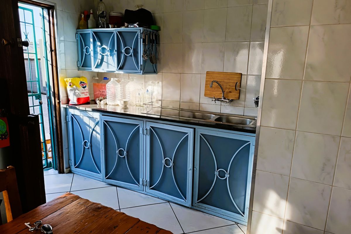 A functional kitchen area featuring blue built-in cabinetry, a double bowl sink, and tiled splashbacks with direct access to an exterior security gate.