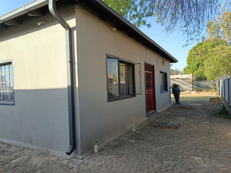 Rear exterior view of the property featuring a paved courtyard, metal security gate, and functional rainwater gutter system.