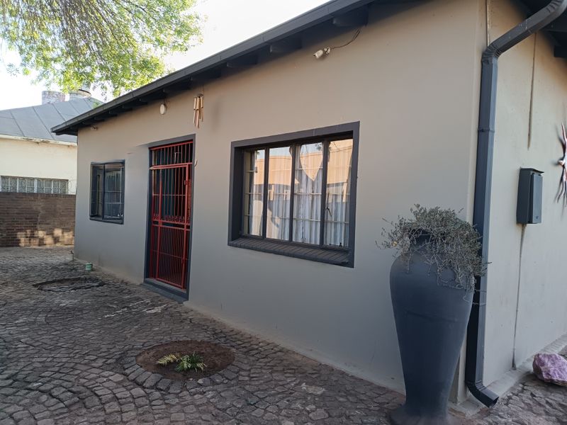 Rear exterior view of the house featuring painted masonry walls, metal security gate, and cobblestone paving.