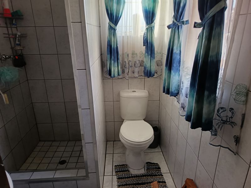 A functional bathroom featuring a tiled shower enclosure and a standard toilet with neutral wall and floor tiling.