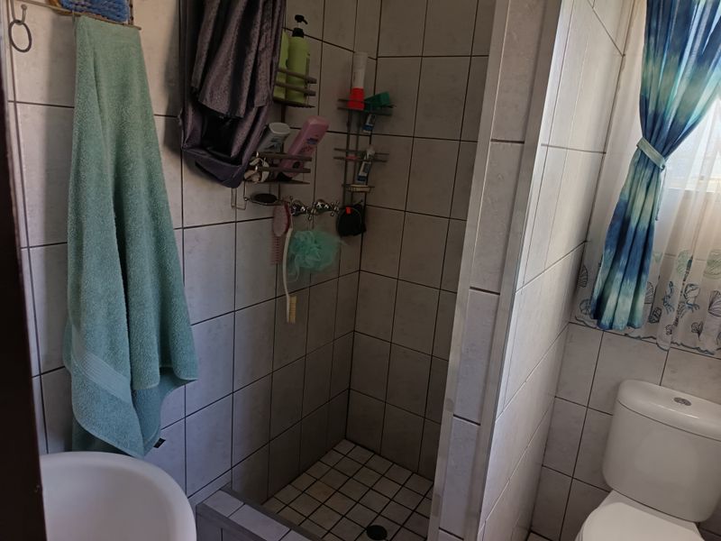 A functional bathroom featuring a tiled shower enclosure and a standard toilet, with dated wall tiling and visible grout wear.
