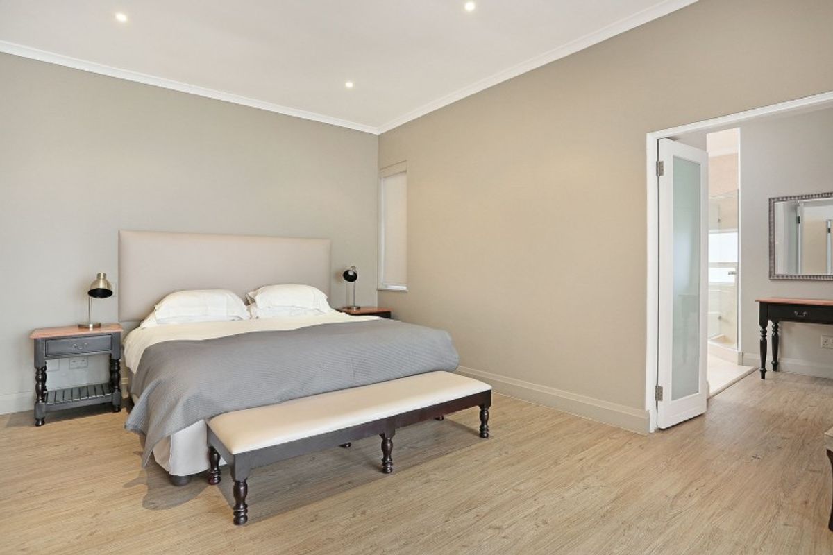Spacious bedroom featuring neutral walls, recessed downlights, and laminate flooring, with an adjoining ensuite bathroom accessible through a frosted glass door.