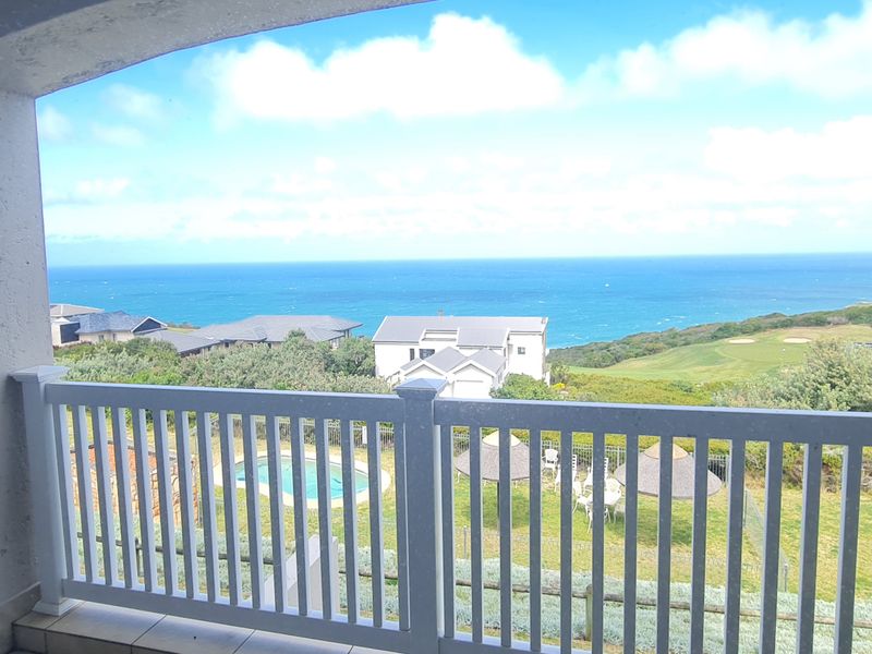 A covered balcony featuring a white balustrade and tiled flooring, offering expansive views of the ocean and surrounding landscape.