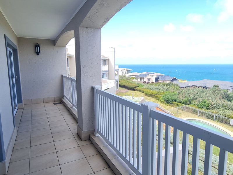 A spacious covered balcony featuring tiled flooring, white balustrades, and arched pillars, offering expansive coastal and ocean views.
