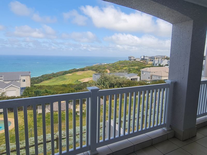 Spacious covered balcony featuring tiled flooring and a white balustrade, offering expansive coastal and golf course views.