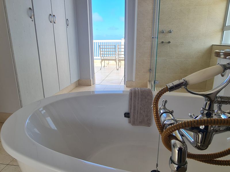 Spacious bathroom featuring a freestanding bathtub, chrome fixtures, built-in cabinetry, and direct access to a private balcony with ocean views.