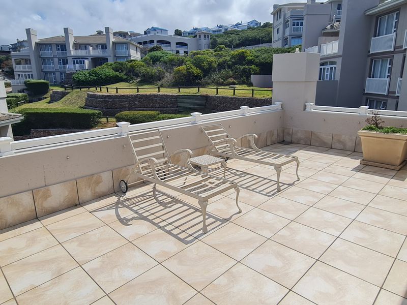Spacious open-air balcony featuring tiled flooring and a protective balustrade, offering views of the surrounding apartment complex and landscaped grounds.