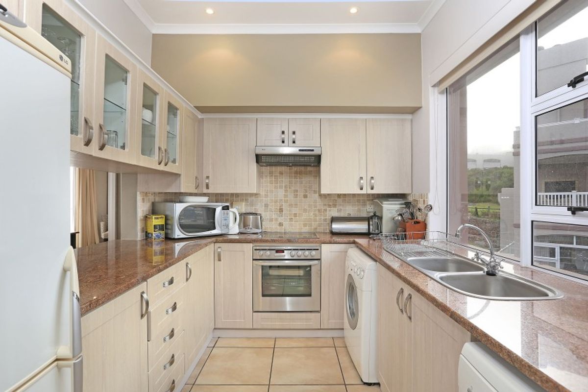 A functional kitchen featuring light wood cabinetry, granite countertops, a mosaic tile backsplash, and integrated appliances including an oven and hob.