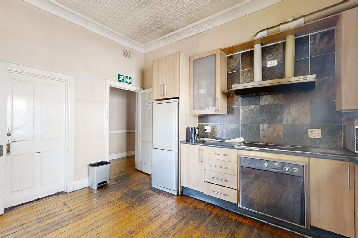 A functional kitchen featuring built-in cabinetry, integrated oven and hob, tiled backsplash, and original timber flooring with a decorative ceiling.