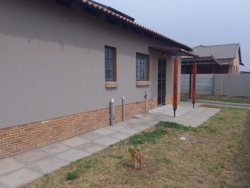 Rear exterior view of the townhouse featuring a paved walkway, covered patio area, and brick-accented facade with security gate.