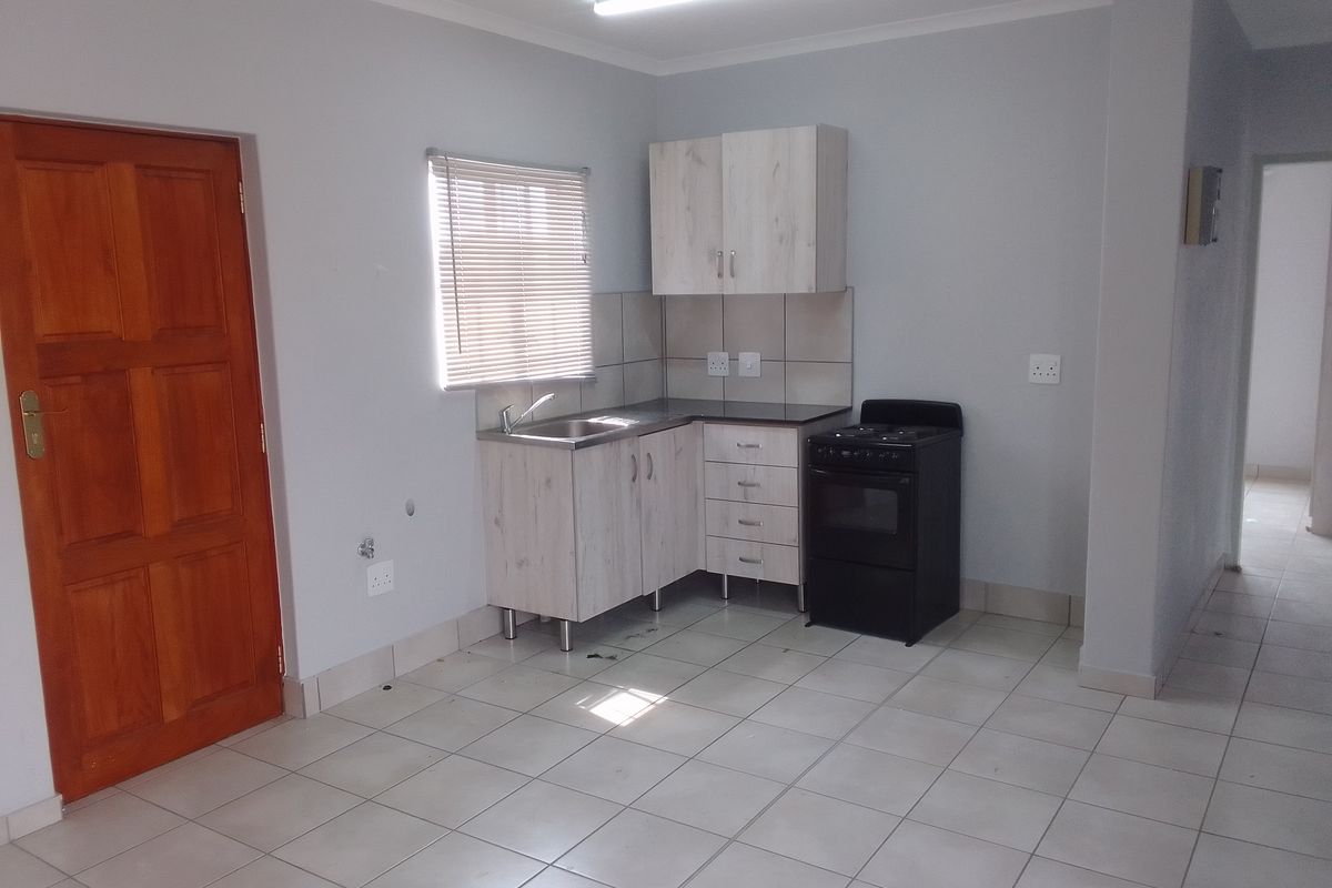 A compact kitchen area featuring light wood-finish cabinetry, a stainless steel sink, tiled splashbacks, and a freestanding stove.