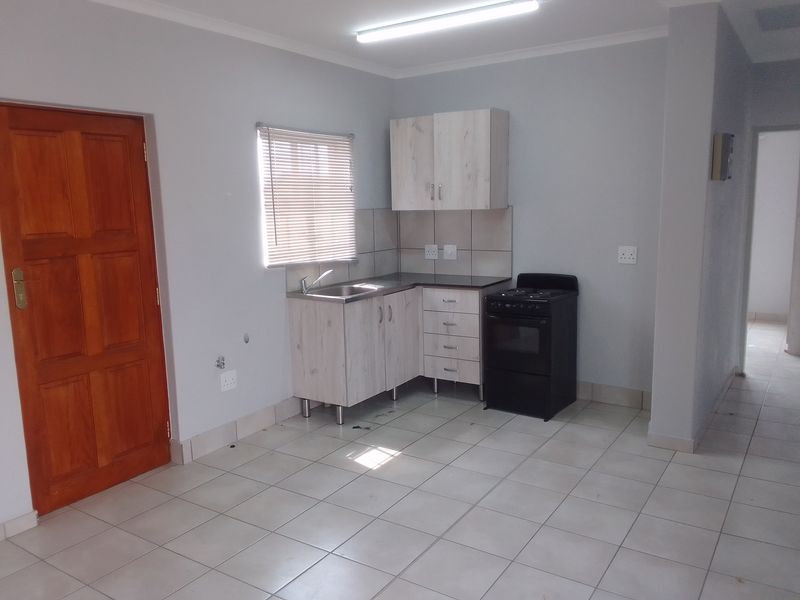 A compact kitchen area featuring light wood-finish cabinetry, a stainless steel sink, tiled splashbacks, and a freestanding stove.