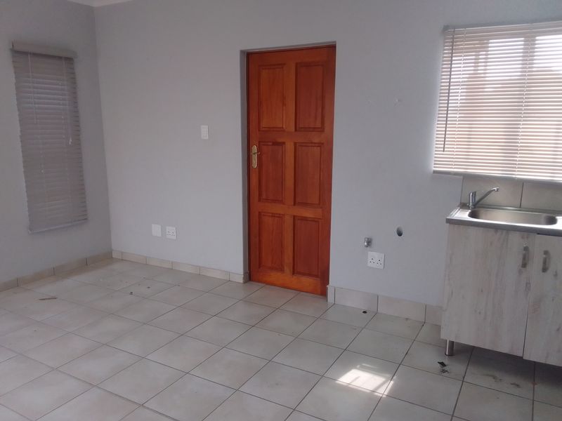 A functional kitchen area featuring tiled flooring, a single basin sink with cabinetry, and venetian blinds on the windows.