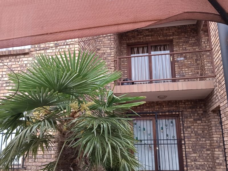 Rear view of a face brick townhouse featuring a private balcony with metal balustrades, security bars on windows, and a shade cloth covered patio area.