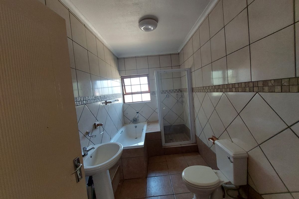 A functional bathroom featuring a pedestal basin, built-in bathtub, separate shower enclosure, and toilet, finished with neutral ceramic wall and floor tiles.