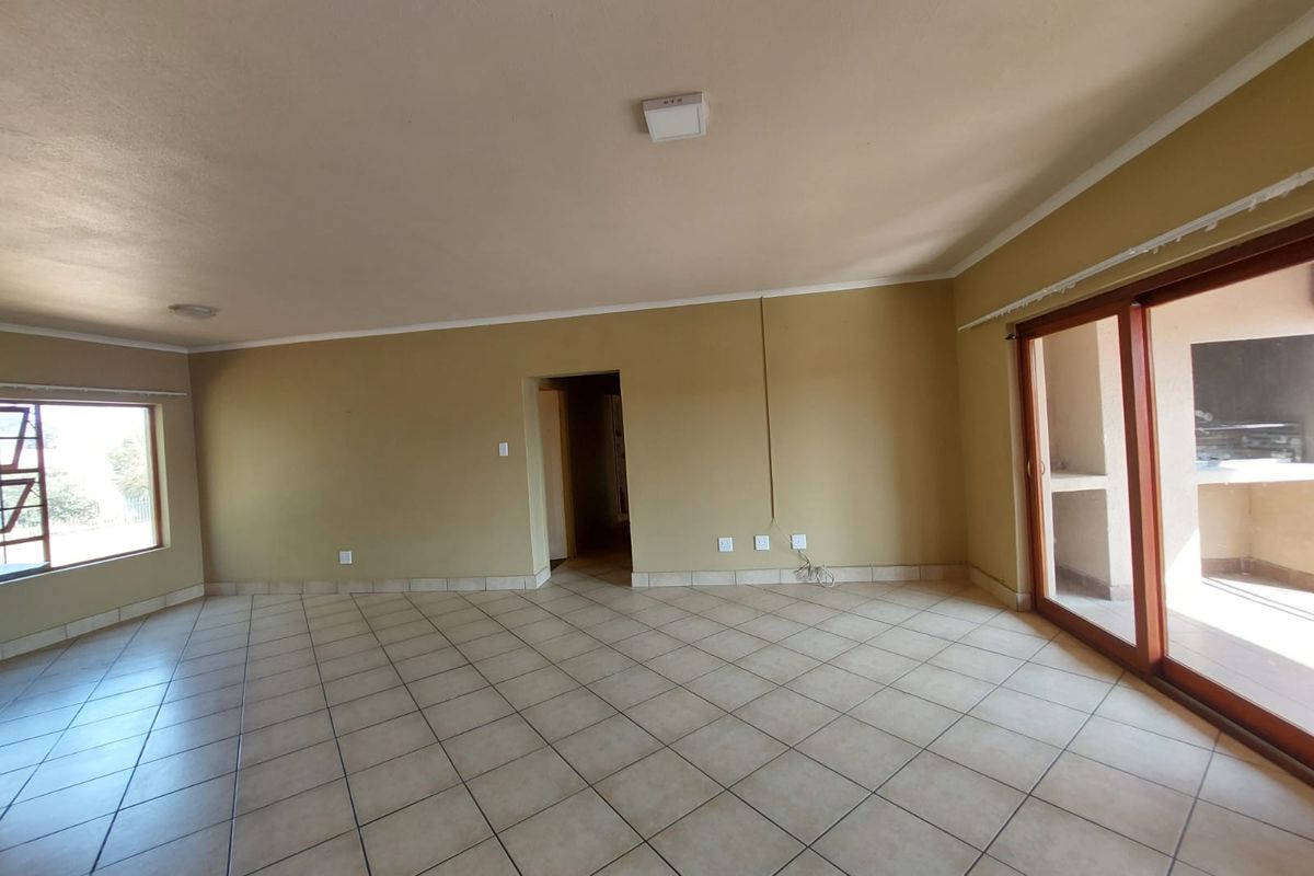 An empty, open-plan living area featuring neutral tiled flooring, a sliding glass door leading to a patio, and simple ceiling lighting.