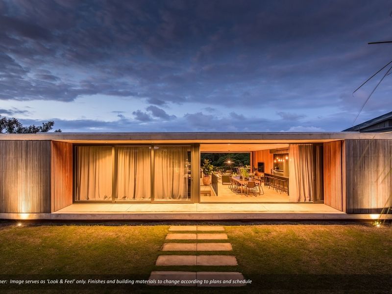 Modern rear facade featuring expansive sliding glass doors, timber cladding, and a covered concrete patio overlooking the garden at dusk.