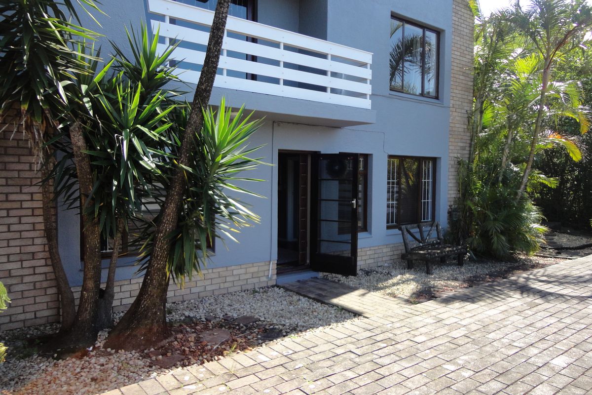 Rear exterior view of the townhouse featuring a paved courtyard, established garden, and a private balcony with white railing.