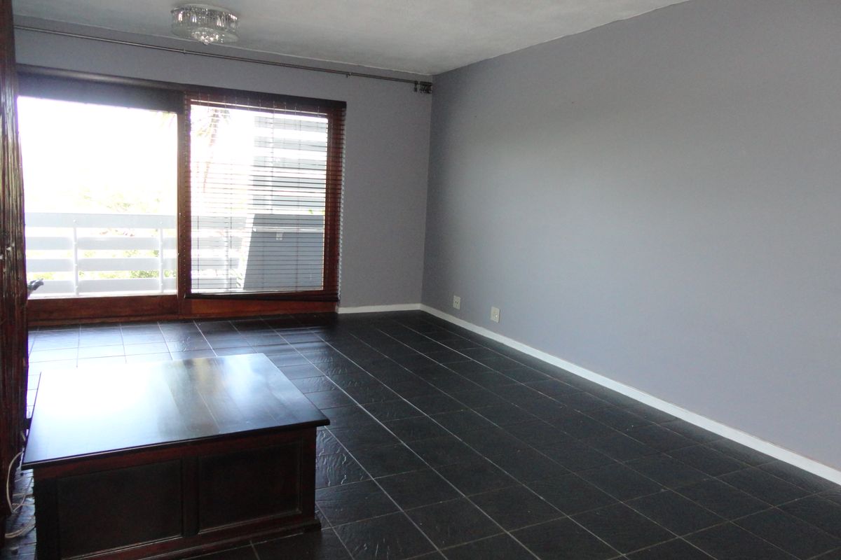 A spacious living room featuring dark slate floor tiles, grey walls, and large sliding glass doors leading to an outdoor balcony area.