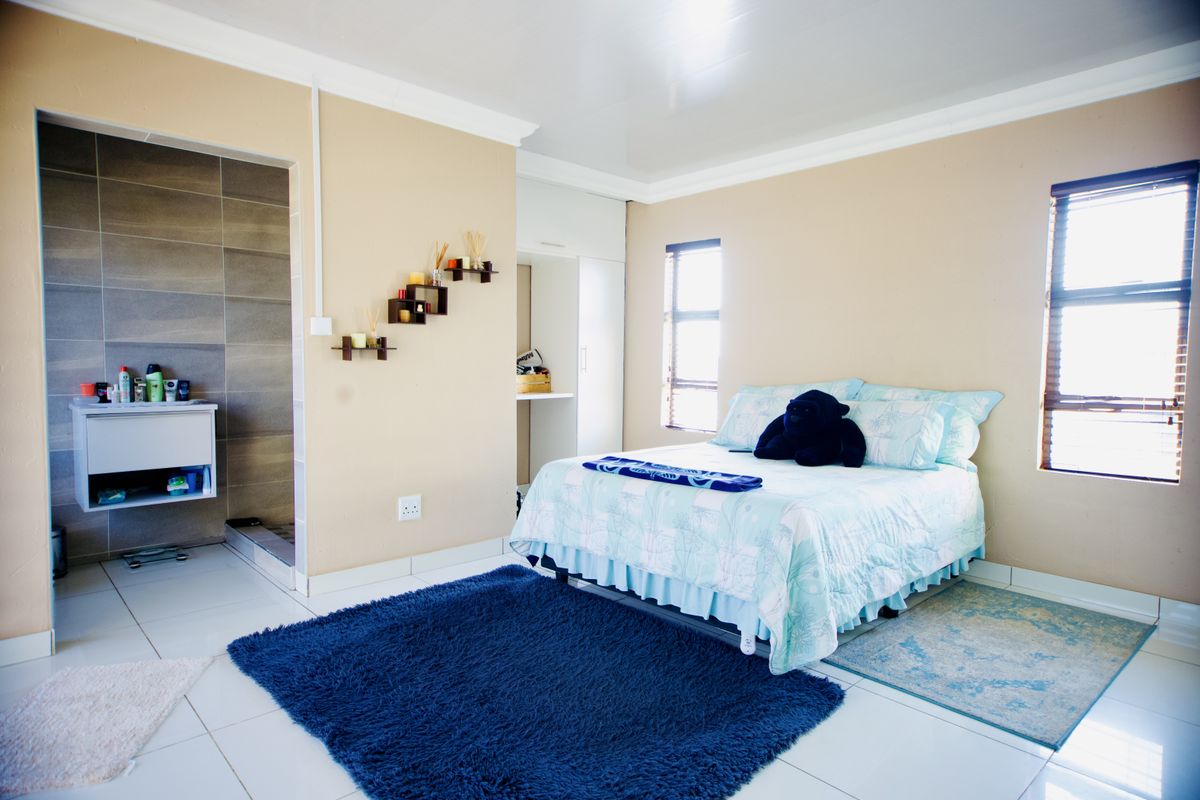 A spacious bedroom featuring tiled flooring, built-in wardrobe storage, and an adjoining en-suite bathroom with modern wall tiling.