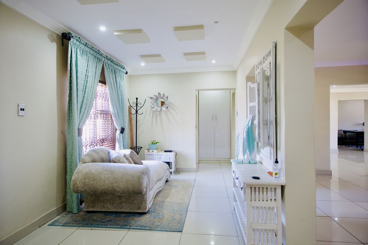 A bright living area featuring polished tiled flooring, recessed ceiling detailing, and a built-in storage cupboard, offering a clean and functional layout.