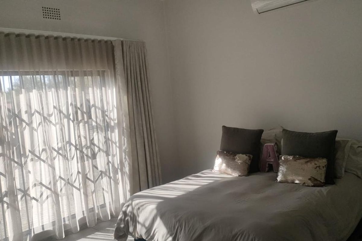 A bright bedroom featuring a large sliding glass door with security gate, neutral wall finishes, and a wall-mounted air conditioning unit.