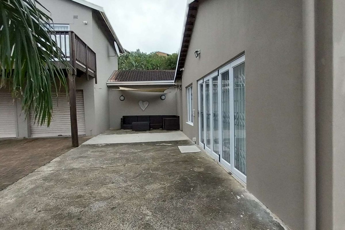 Rear exterior view featuring a concrete driveway, double garage, and access to the main living area through folding glass doors with security gates.