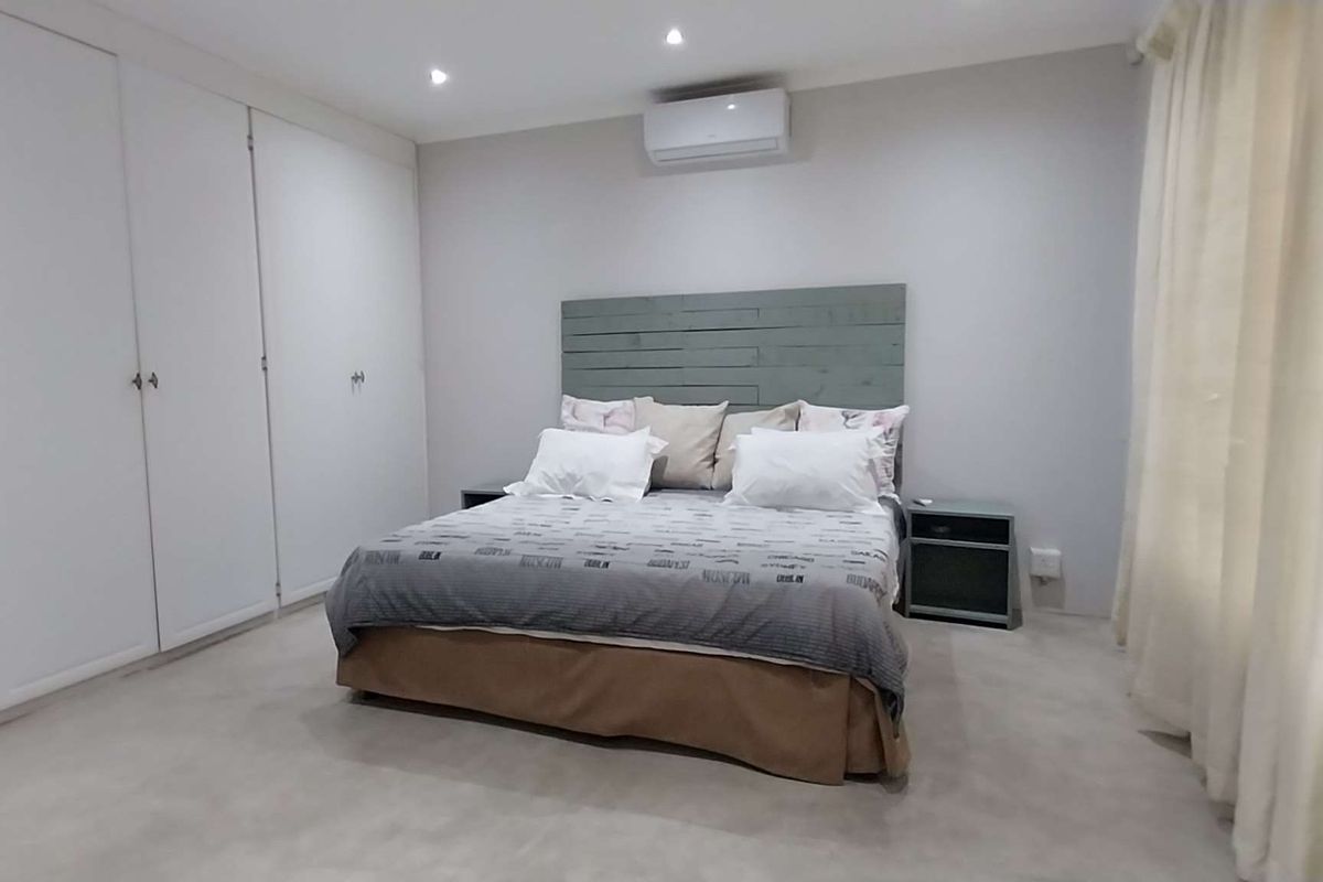 Spacious bedroom featuring extensive built-in cupboards, recessed downlighting, and a wall-mounted air conditioning unit for climate control.