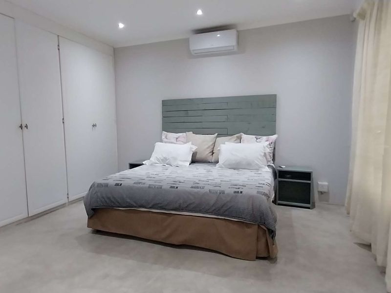 Spacious bedroom featuring extensive built-in cupboards, recessed downlighting, and a wall-mounted air conditioning unit for climate control.