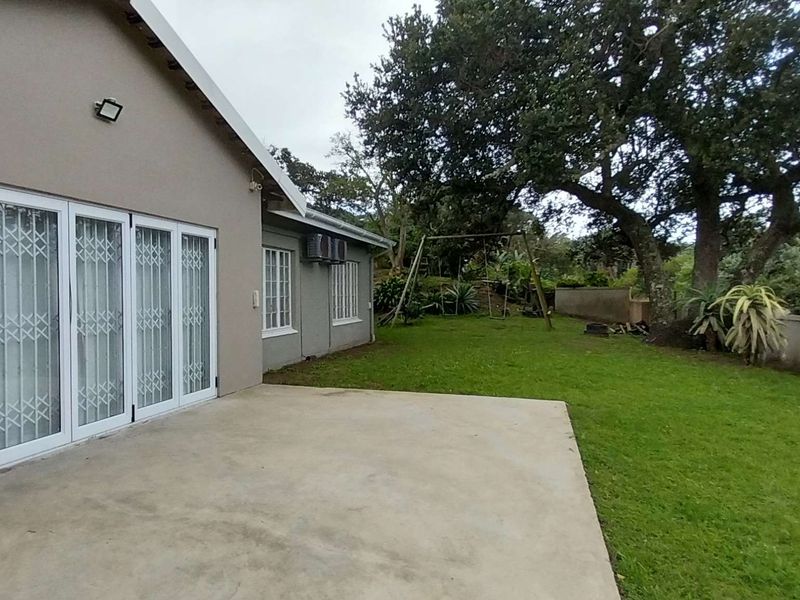 Rear view of the property featuring a concrete patio, sliding glass doors with security gates, and a spacious garden with a boundary wall.