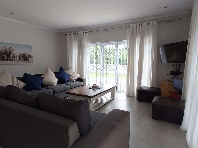 A comfortable living room featuring tiled flooring, recessed downlights, and double glass doors leading to the exterior, secured with a metal gate.
