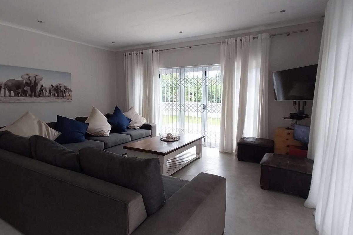 A comfortable living room featuring tiled flooring, recessed downlights, and double glass doors leading to the exterior, secured with a metal gate.