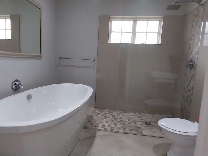 Modern bathroom featuring a freestanding bathtub, a walk-in shower with mosaic tiling, and a toilet, finished with neutral wall tones.
