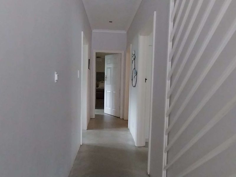 A clean, neutral-toned hallway featuring recessed downlights and multiple internal doors leading to various rooms within the home.