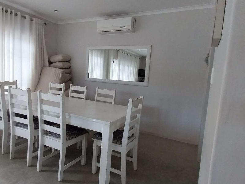 A bright dining room featuring a wall-mounted air conditioning unit, recessed lighting, and large windows with curtain tracks.