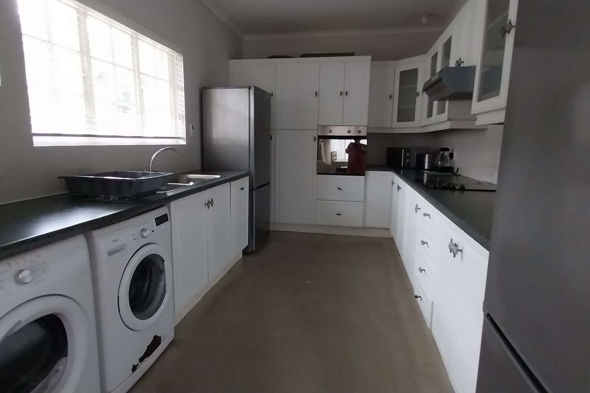 Functional kitchen featuring white cabinetry, dark countertops, integrated oven, extractor fan, and dedicated space for laundry appliances under the counter.